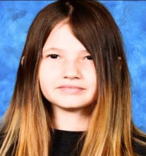 young girl with long brown hair gives a subdued smile